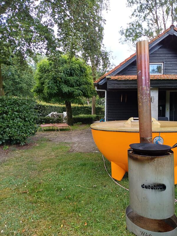 Oranje Dutchtub met de houtkachel op de voorgrond, bij een zwart houten huisje