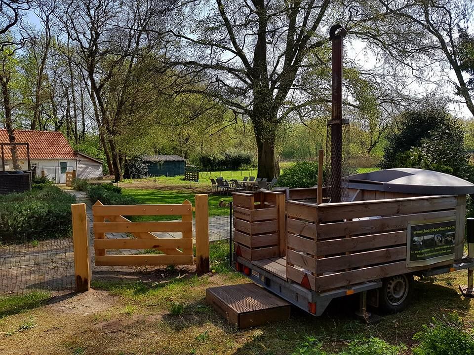 De vaste houten hottub op zijn aanhanger, met schoorsteen, in een tuin onder hoge bomen